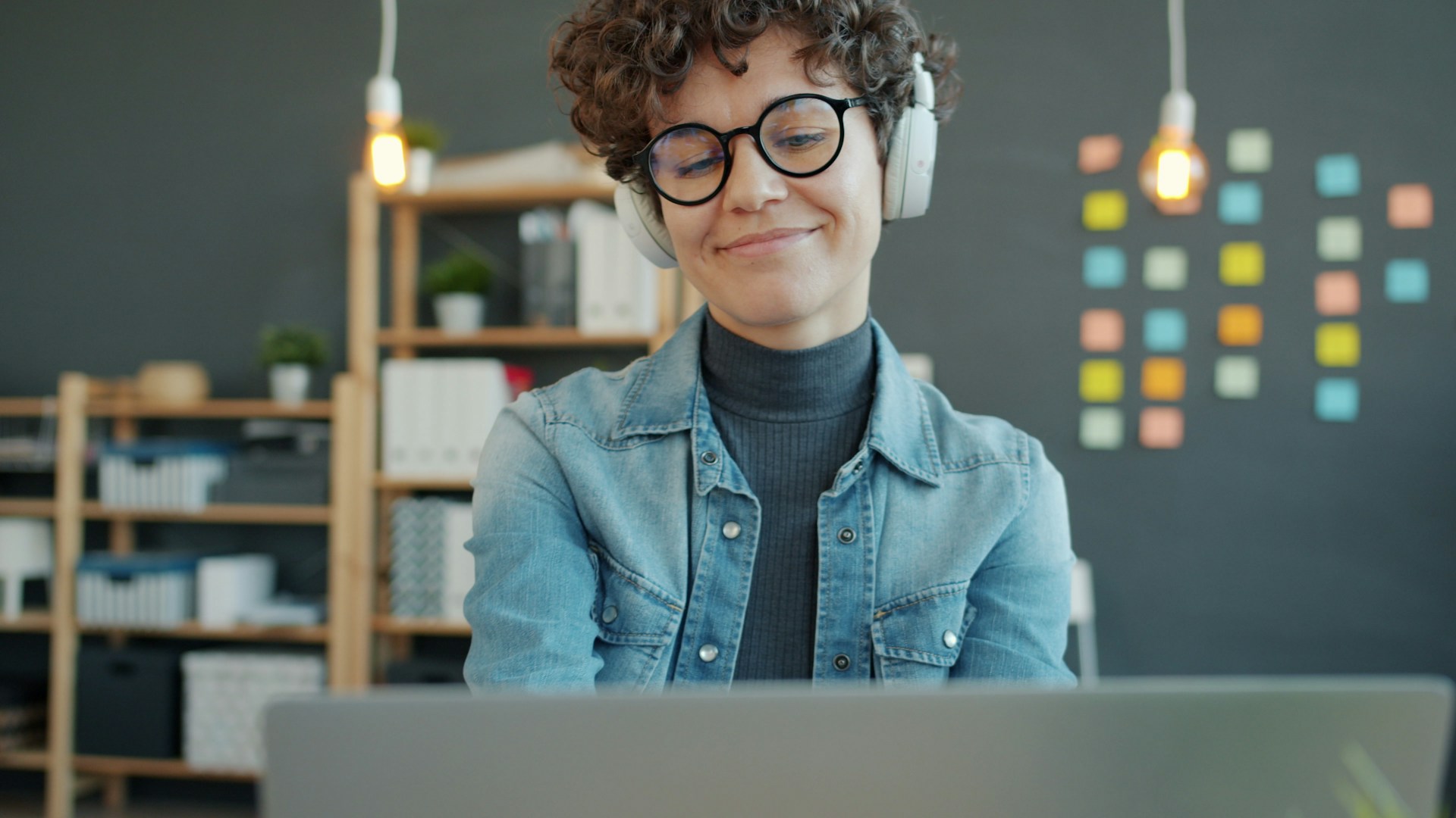 Podcaster wearing headphones smiling while working on a laptop